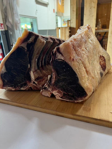 Two bone-in beef cuts, showcasing the characteristic crust and marbling of dry-aged beef, are displayed on a wooden board. Indulge in the luxury of dry-aged beef, aged in the comfort of your own home.